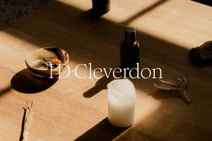 Wooden tabletop styled with a ceramic bowl, dropper bottle, and candle under natural sunlight with H.D. Cleverdon typography