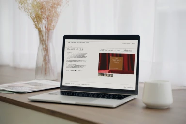 A modern laptop computer displaying an e-commerce website on a wooden tabletop with a vase and mug.