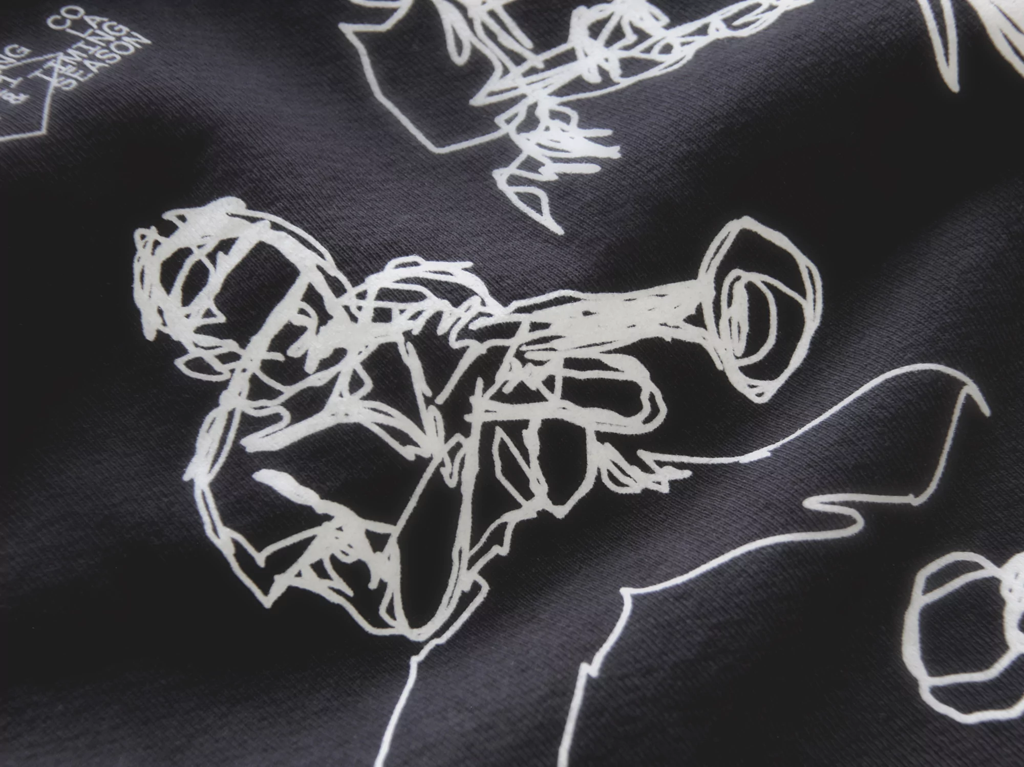 Close-up of a black fabric printed with sketchy white illustrations of jazz musicians playing trumpet and other instruments.