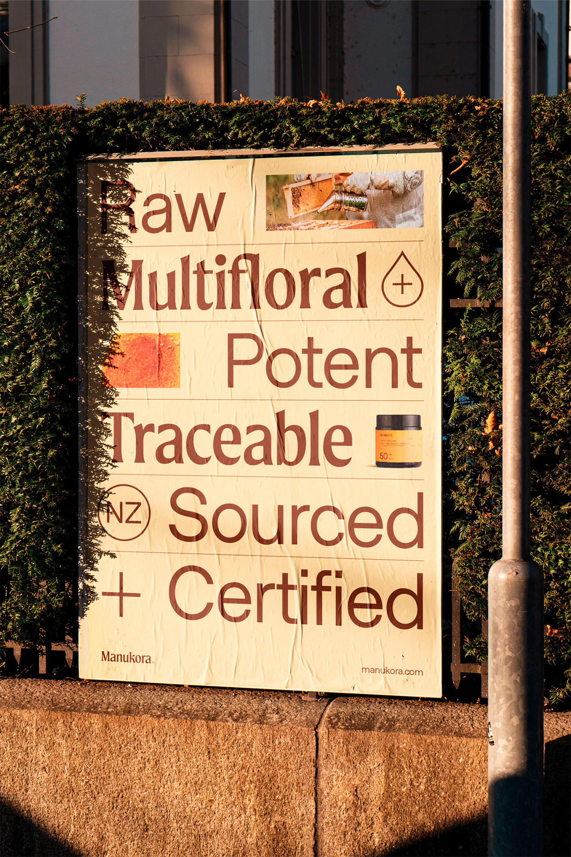 Promotional poster for Manuka honey on a wall with text reading 'Raw Multifloral Potent Traceable Sourced + Certified'.