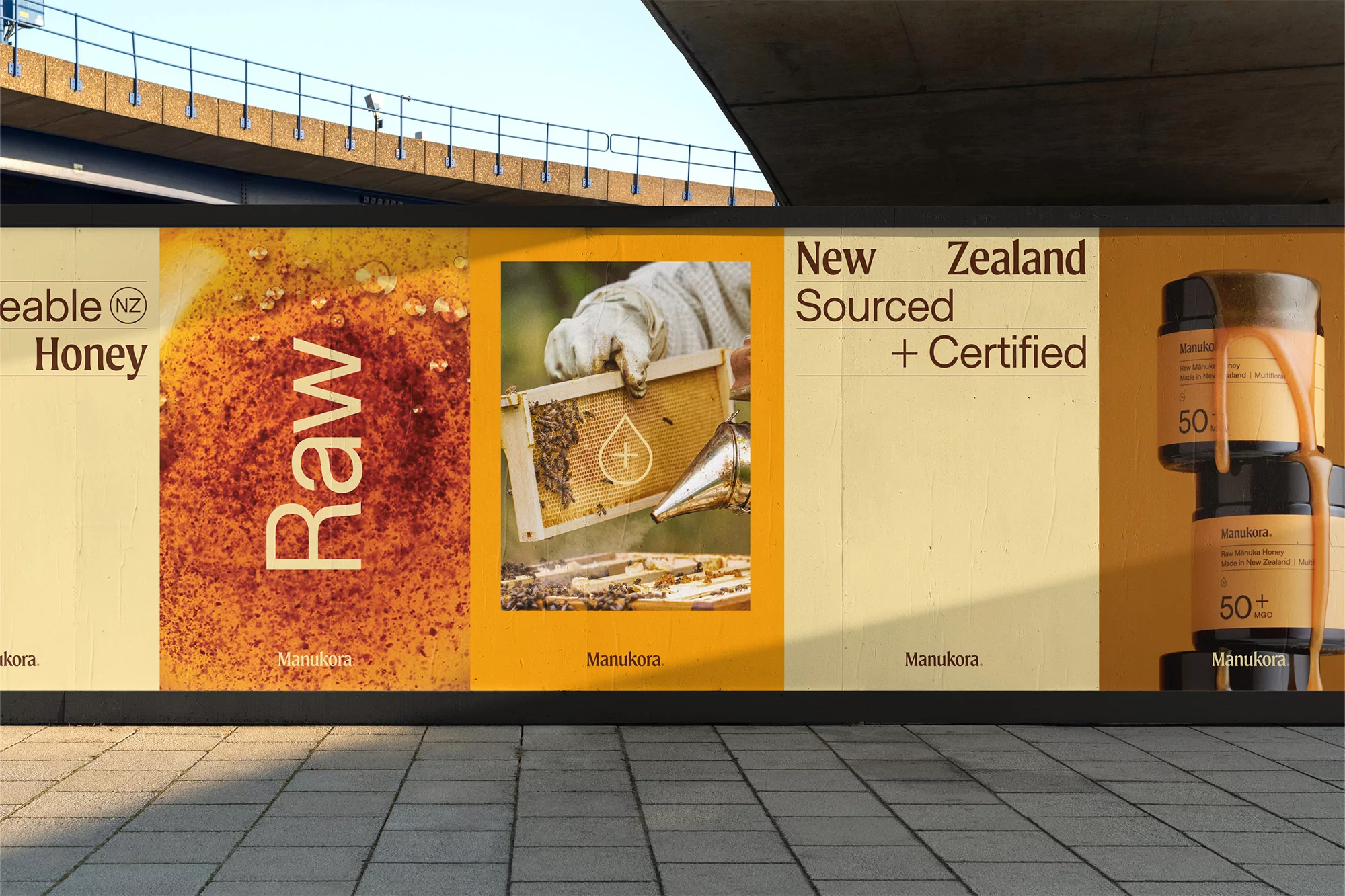 Eye-level outdoor shot of a billboard advertisement featuring honey and honey-related imagery with the brand 'Manukora' displayed.