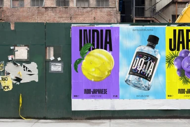 Colorful advertising posters for DOJA gin pasted on a weathered green construction fence on an urban street.