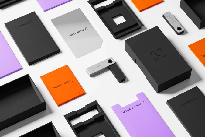 Ledger Nano X crypto wallet and packaging, including accessories and recovery sheet, flat lay on a white background.