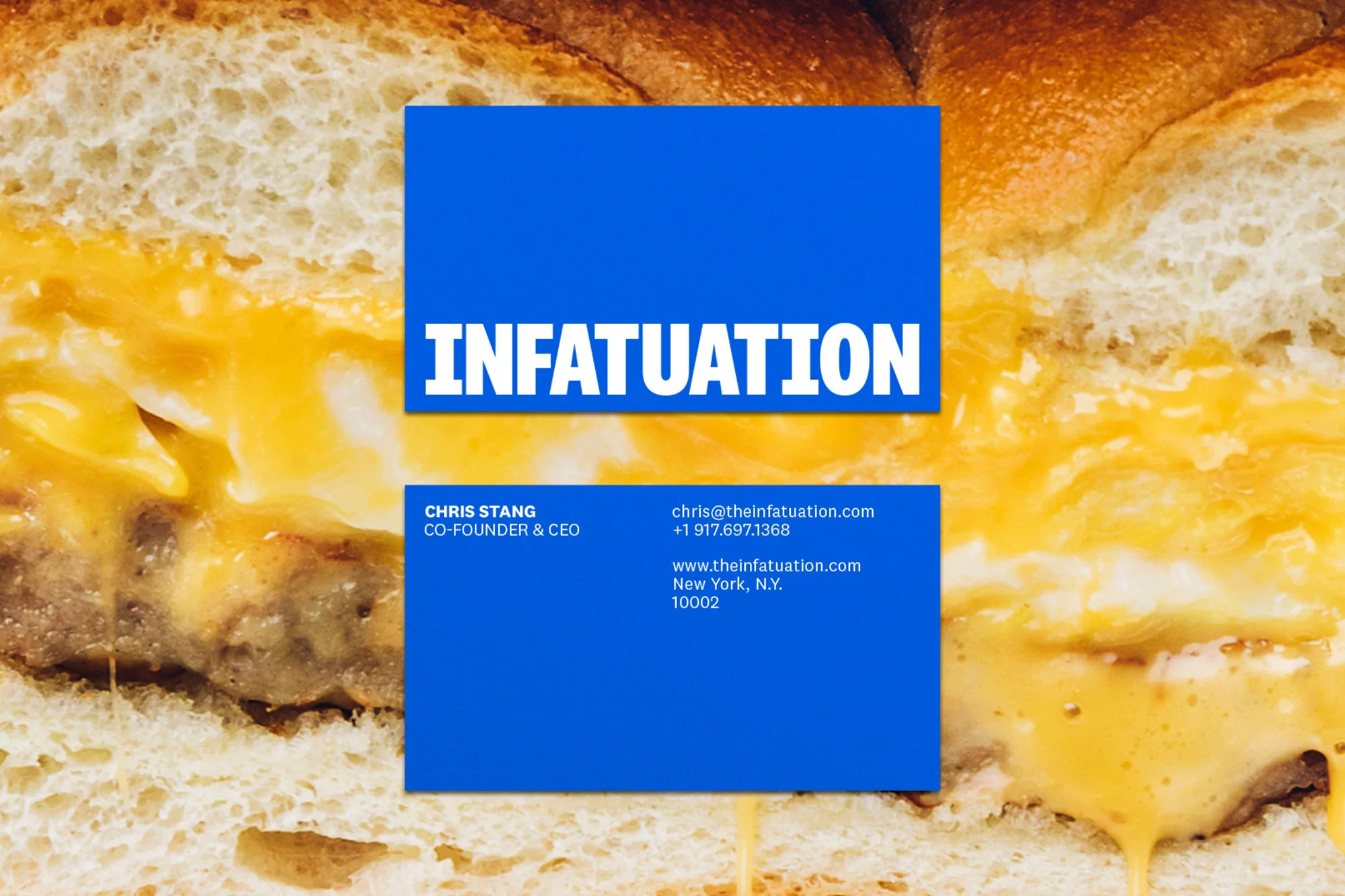 Food photography featuring a sandwich with melting cheese alongside two blue business cards with 'Infatuation' and contact details.
