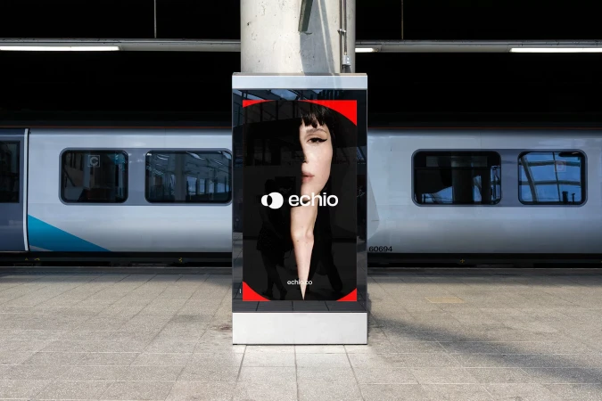 Indoor advertisement featuring a woman's face with Echio logo on display at a train station platform with a passenger train in the background.