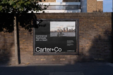 Black advertising poster for Carter+Co mounted on a weathered brick wall showing a city skyline photograph and typography.