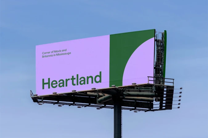 Billboard with a split color block design in light purple and green, displaying the word Heartland in dark green against a blue sky.