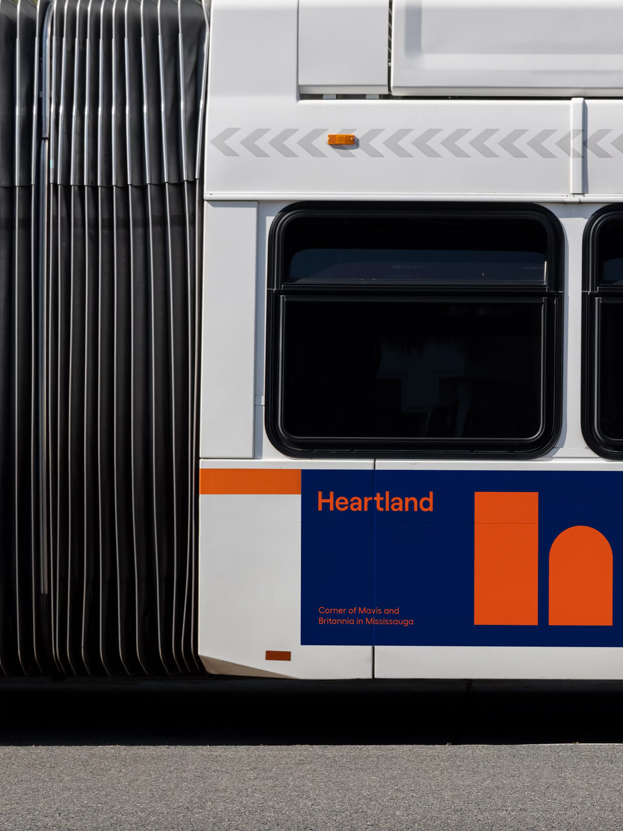 Side view of a white and blue Heartland bus with accordion joint, showcasing the company logo and design elements in a minimalist style.