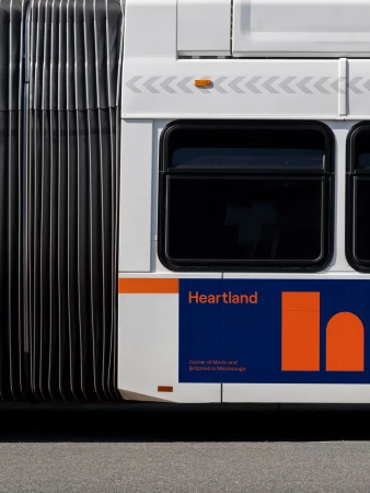 Side view of a white and blue Heartland bus with accordion joint, showcasing the company logo and design elements in a minimalist style.