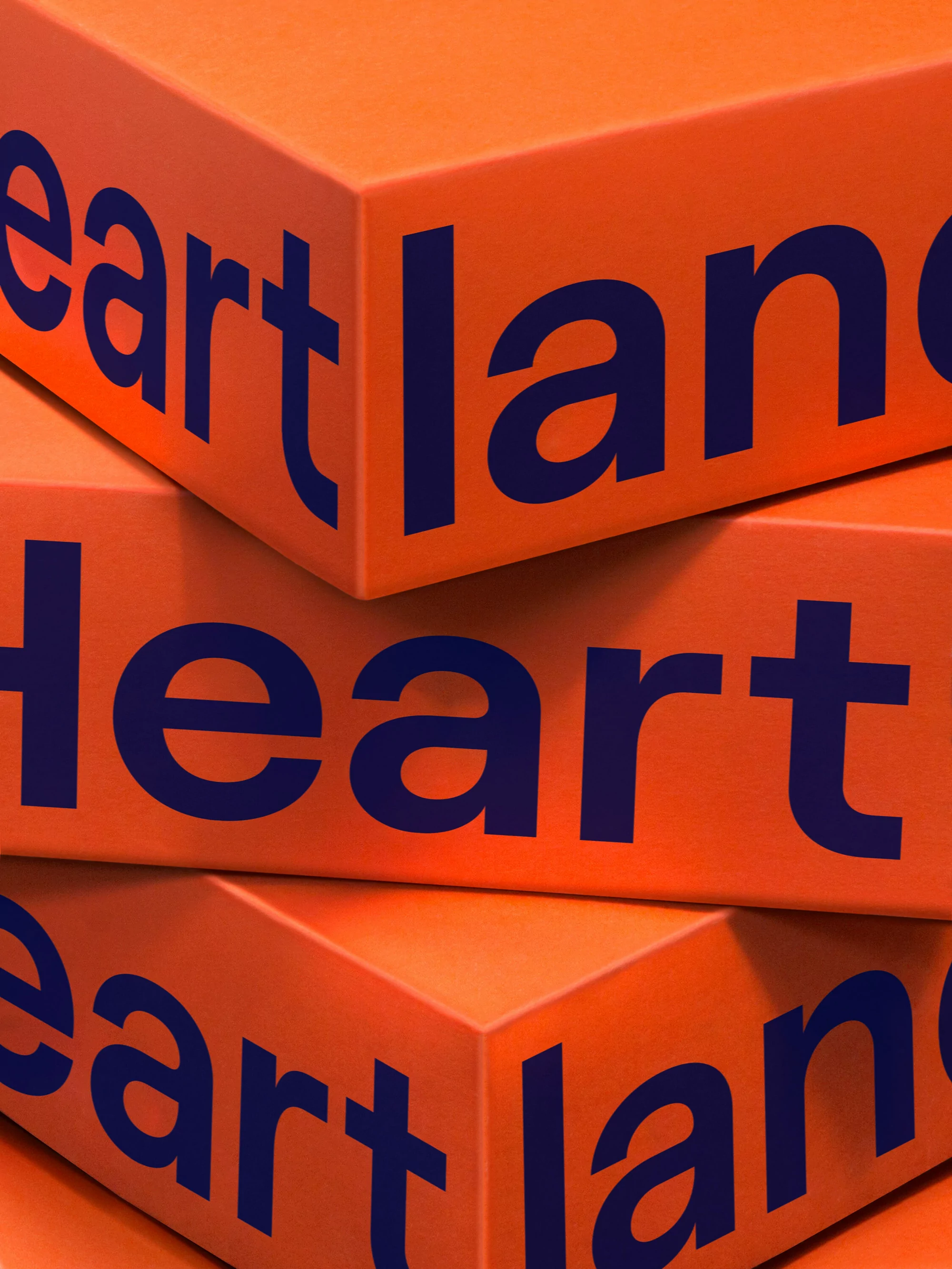 Stacked orange blocks with 'Heartland' in blue text. Geometric shapes form a visually striking text arrangement against a plain background.