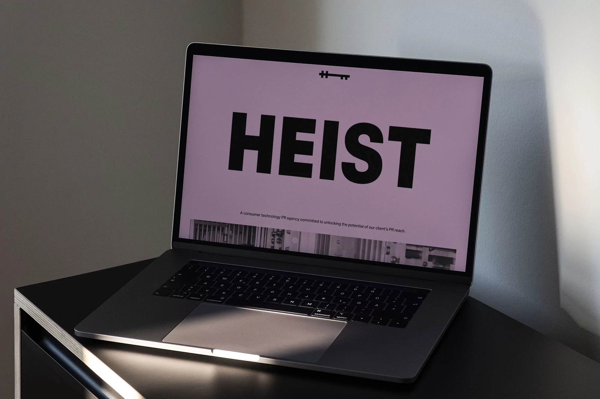 Laptop on a black table displays the word HEIST in large letters on the screen, with a small key symbol above it.