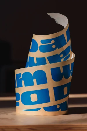Abstract studio shot of paper roll with blue graphic font, neutral background, and shallow depth of field creates a simple yet dynamic composition.