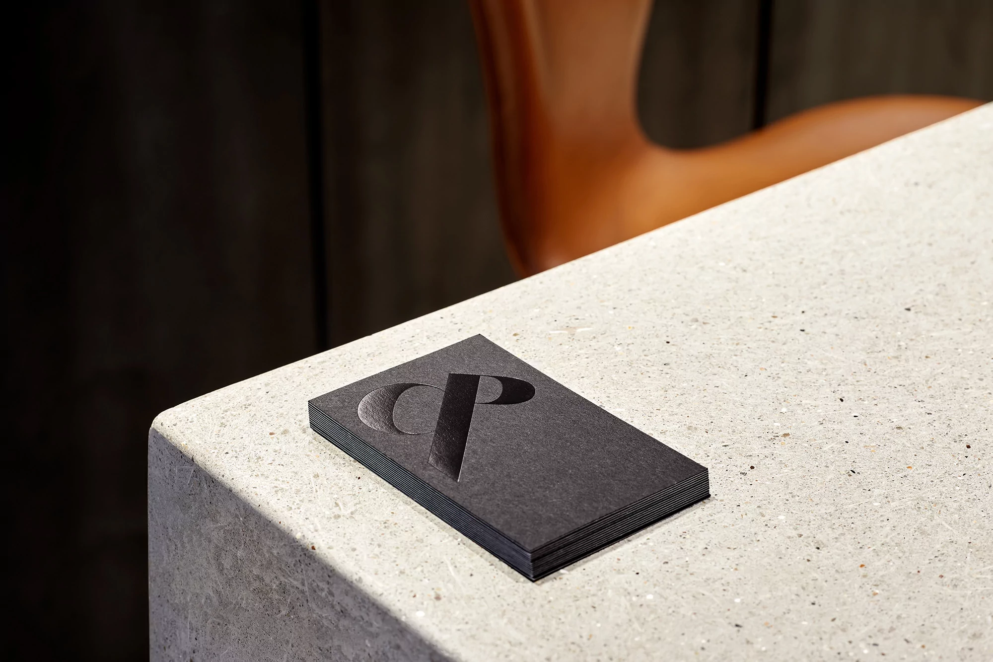 Stack of dark business cards with embossed CP logo on a light speckled surface, featuring a modern, minimalist design.