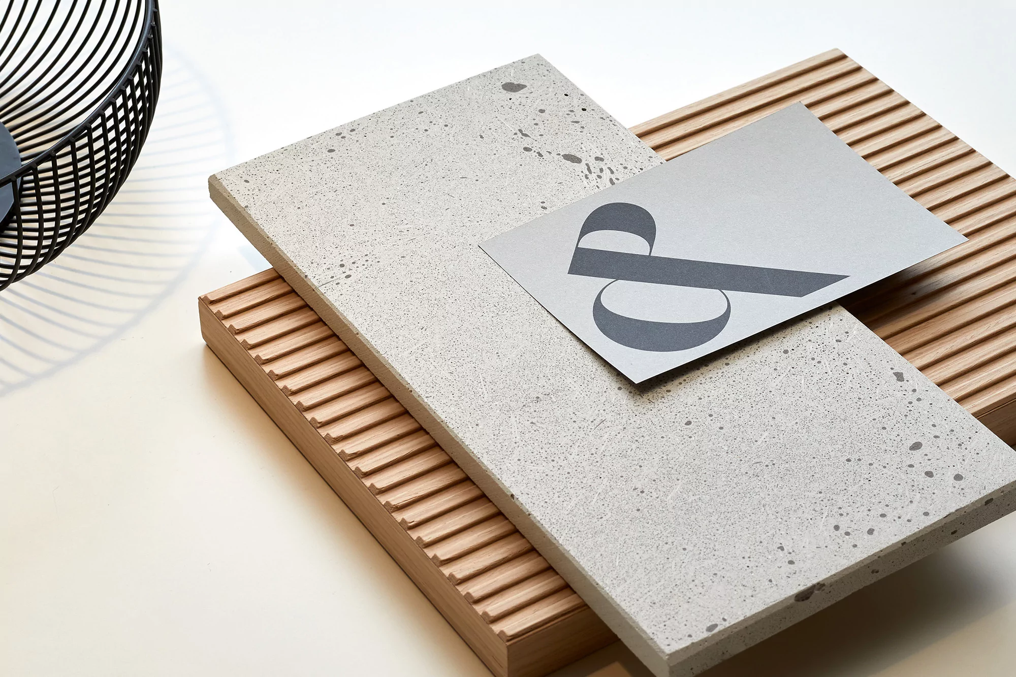 Elevated shot of a concrete slab, wood base, and a card with an abstract design on a white surface, showcasing textures and materials.