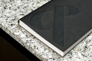 Close-up of a black bound book with debossed CP logo resting on a white and brown terrazzo surface.