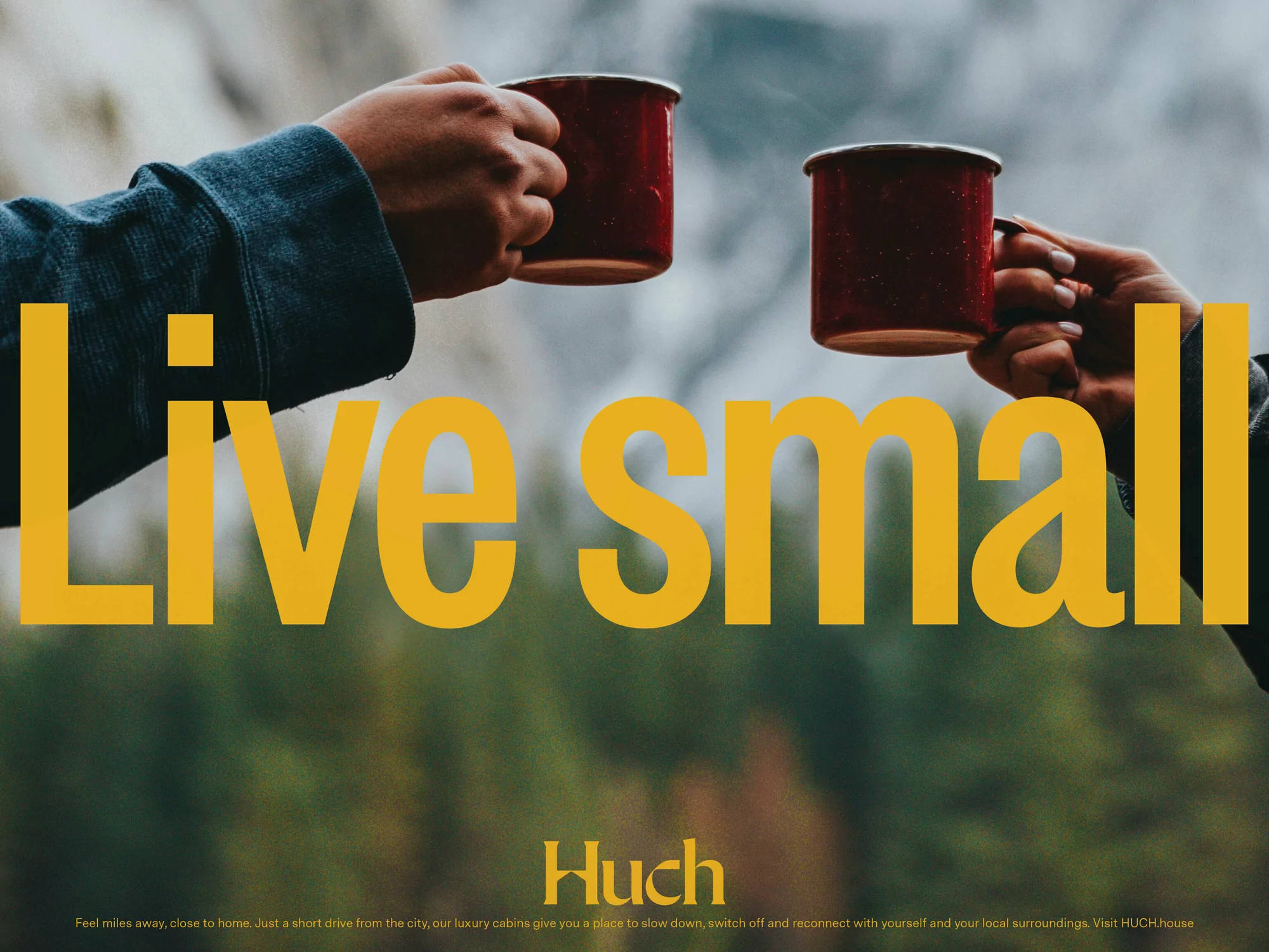 Two red enamel mugs are raised in a toast against a blurred outdoor forest backdrop with the text 'Live Small' overlayed in gold.