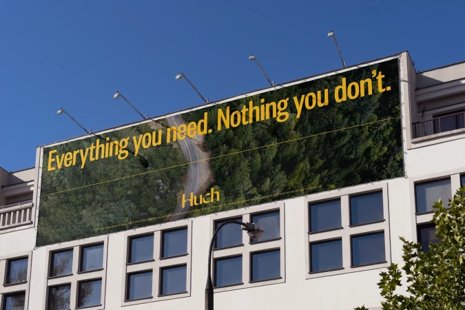 Billboard on a building featuring a green forest road with the text, 'Everything you need. Nothing you don't.', promoting Huch.
