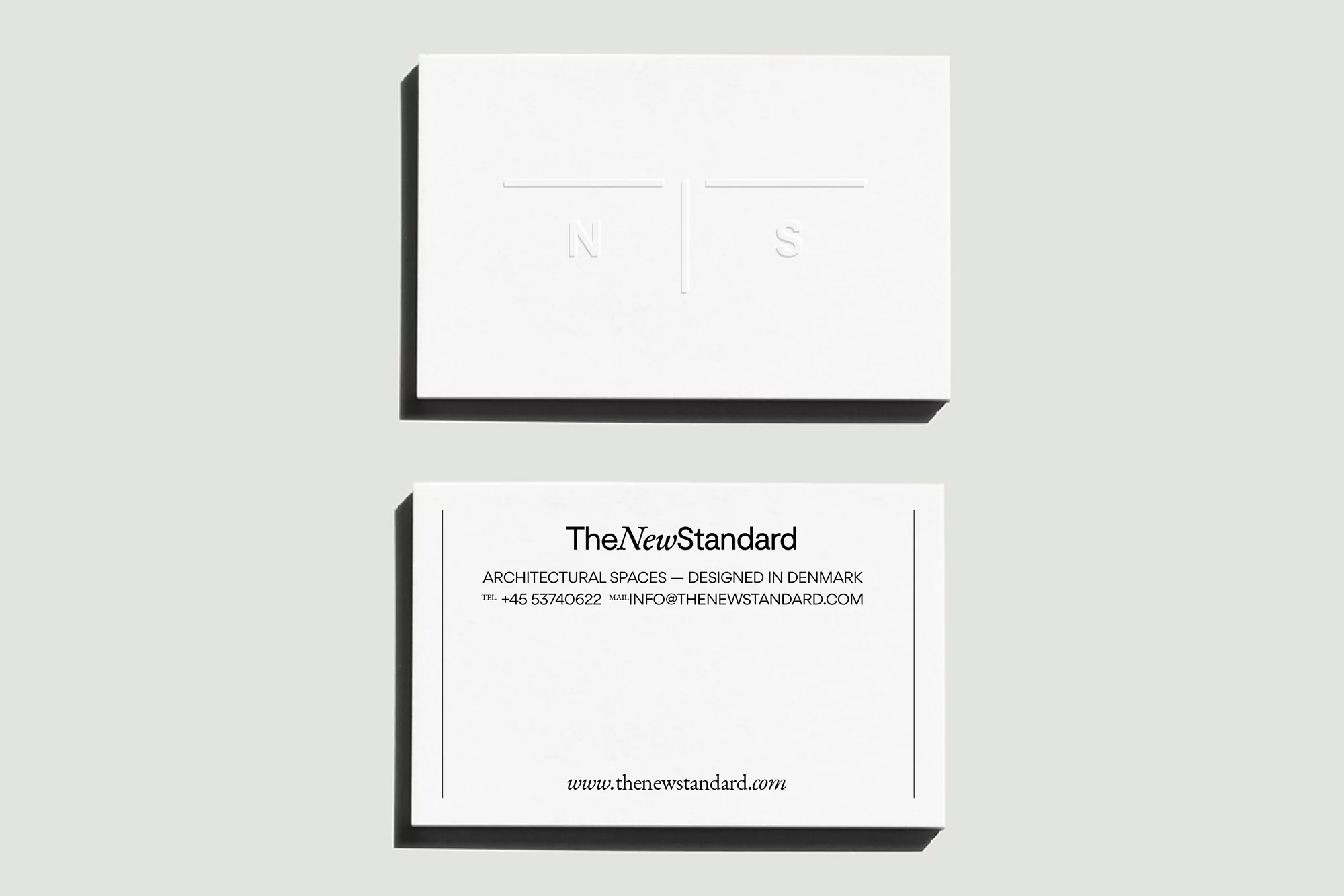 Two white business cards by TheNewStandard featuring a minimalist design with architectural focus and company information.