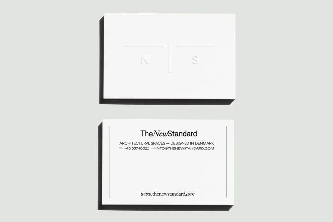 Two white business cards by TheNewStandard featuring a minimalist design with architectural focus and company information.
