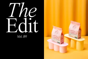 Two pink coffee bags displayed on colourful architectural risers against a warm yellow backdrop with black graphic text on the left.