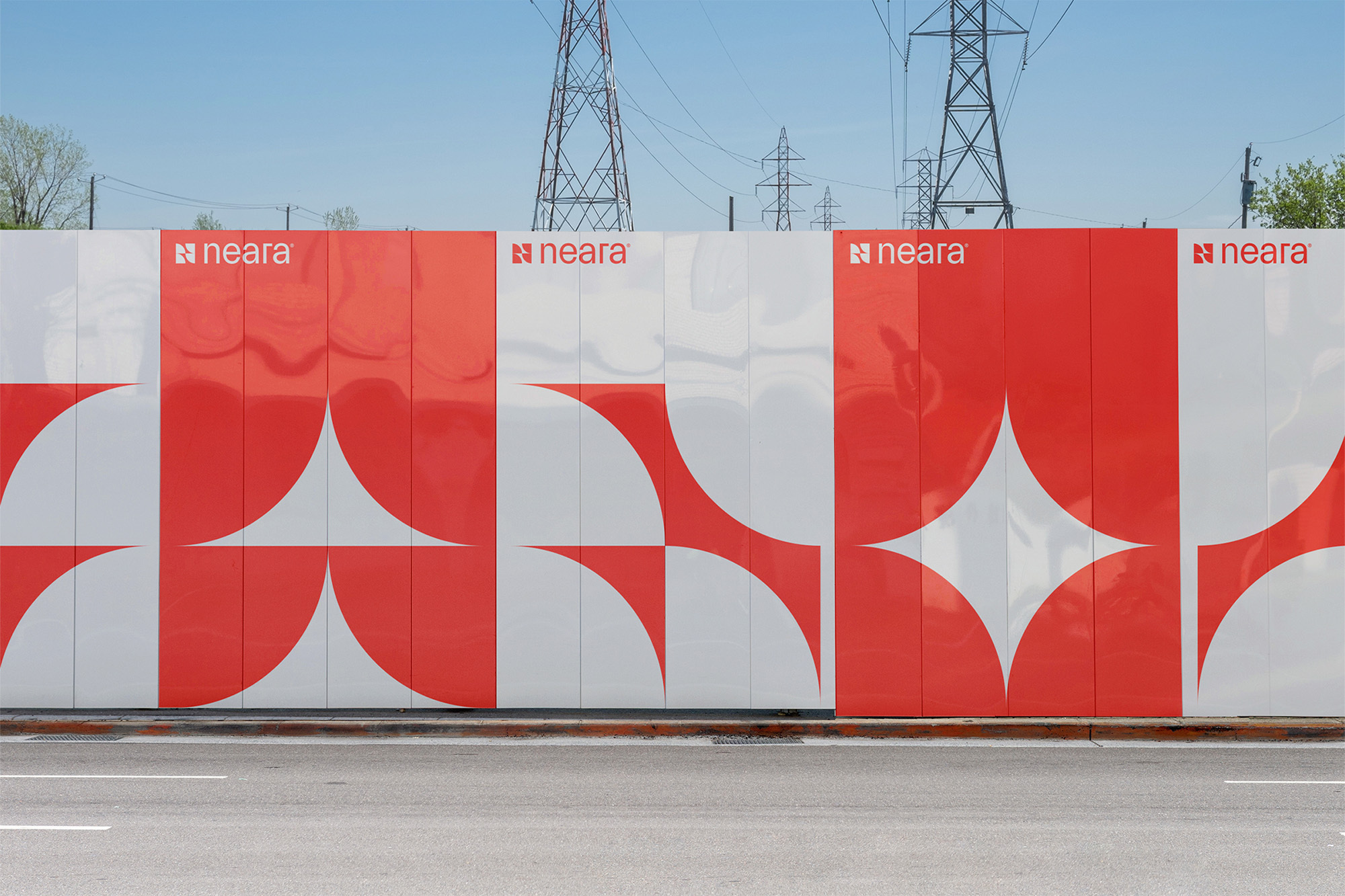 Red and white geometric wall art next to an empty street underneath a blue sky, with tall power lines in the background.
