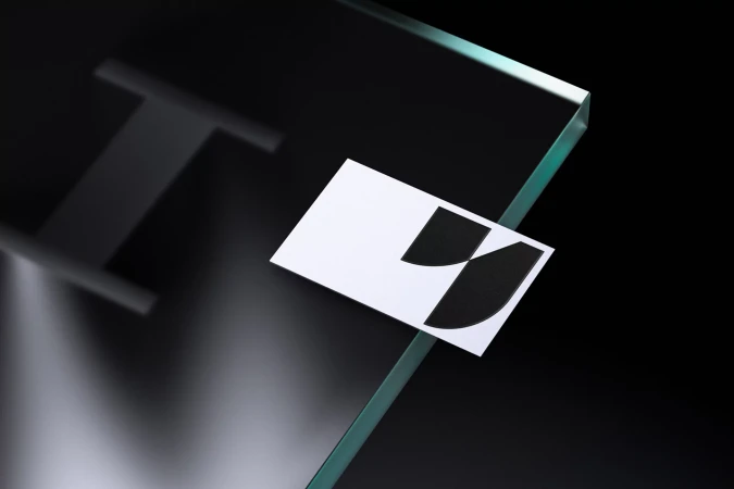 High-angle shot of a business card with an abstract geometric logo on a glossy transparent surface against a stark black backdrop.