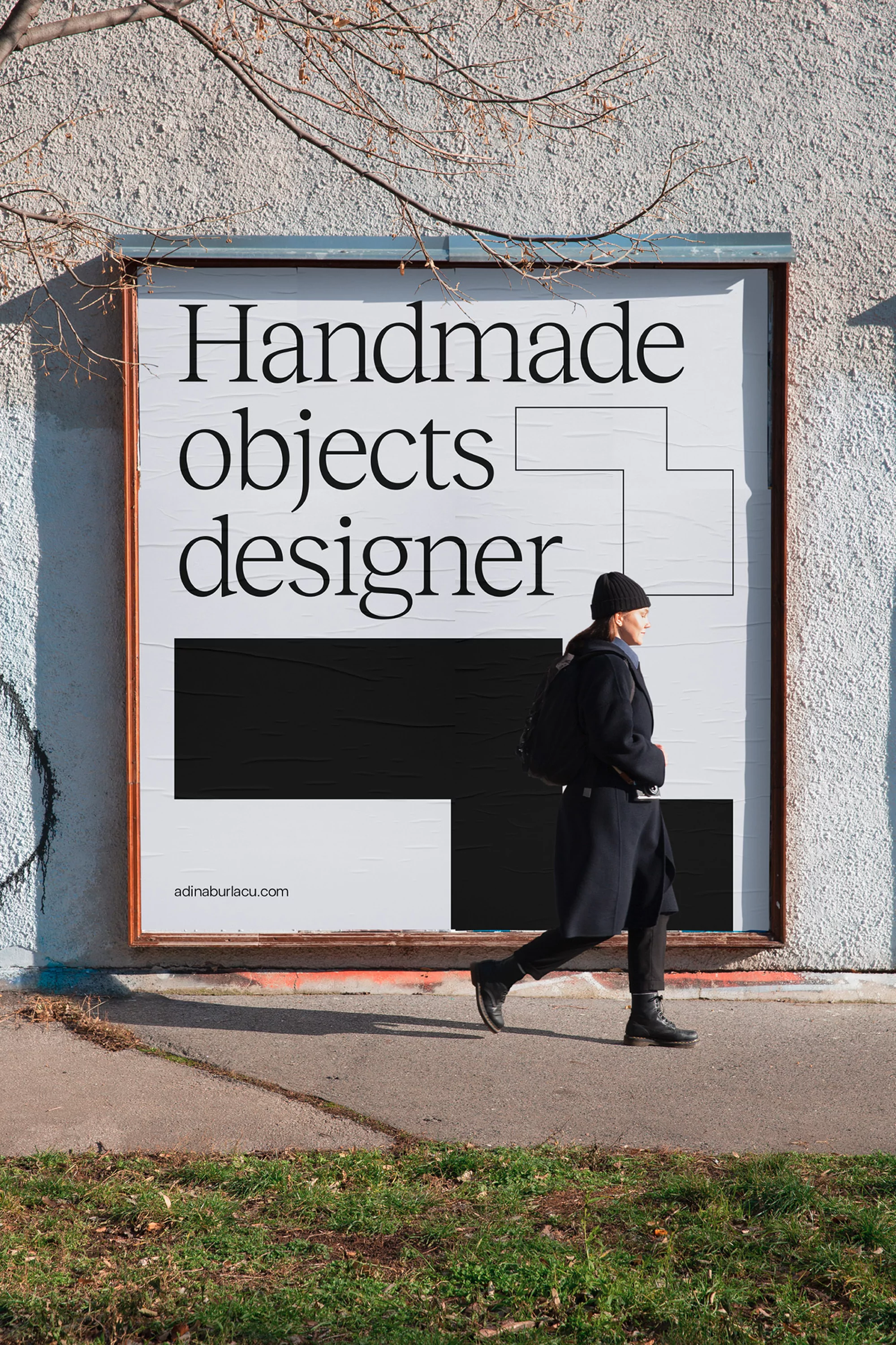Woman walking past an outdoor advertisement featuring the text “Handmade objects designer” against an urban wall in natural light.