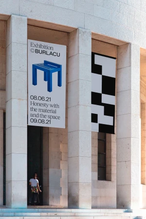 Architectural photo of a building facade with exhibition posters, featuring a person entering the building, under sunlight.