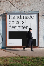 Woman walking past a large outdoor poster featuring typography and abstract shapes on a rough concrete wall.