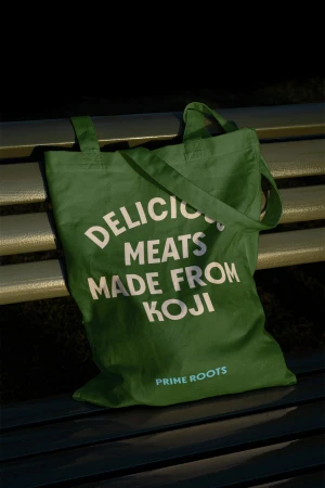 Green canvas tote bag with white typography resting on a dark slatted outdoor bench.