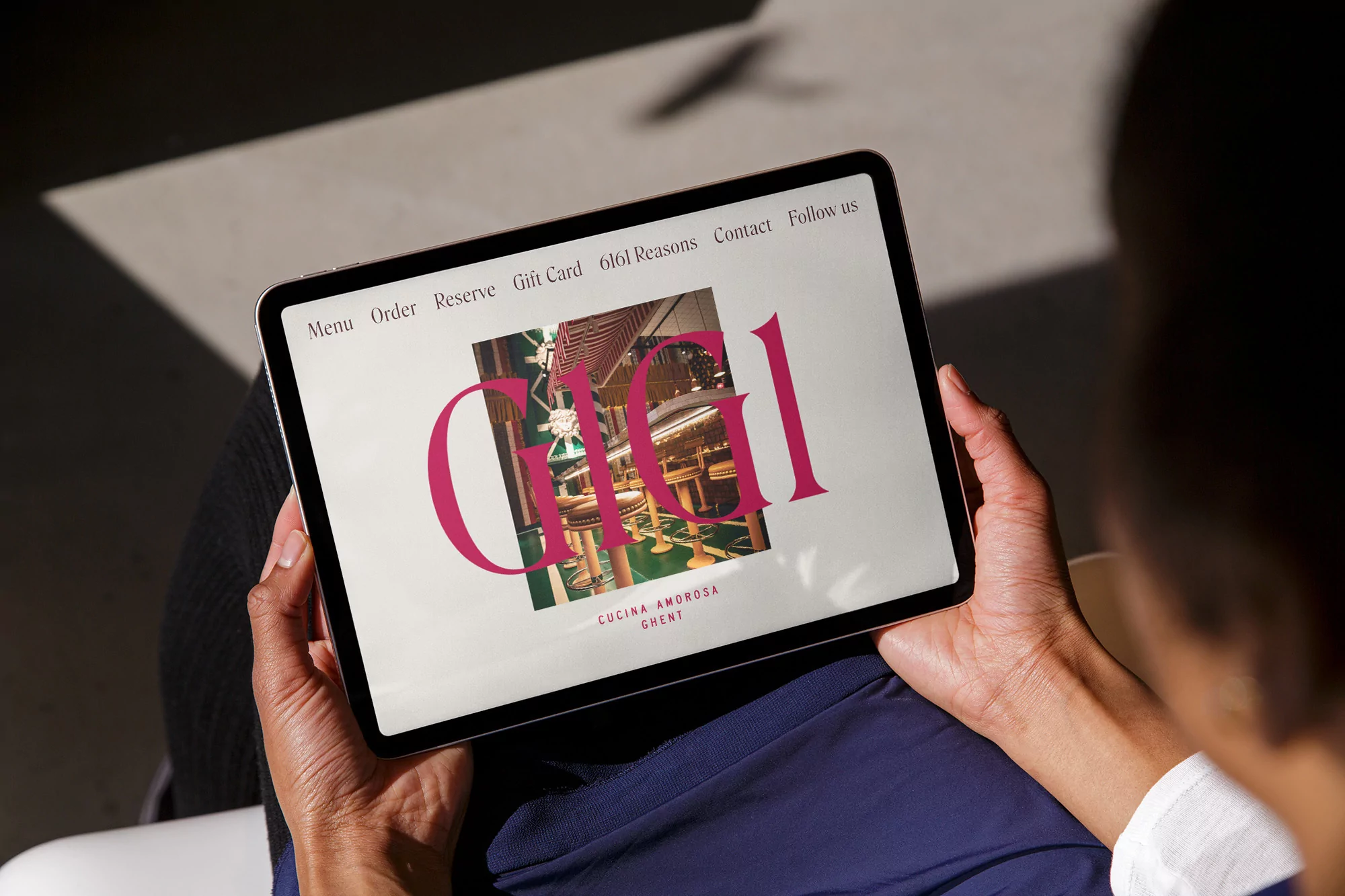 Person holding a tablet displaying the website for Gigi Cucina Amorosa restaurant, featuring a photo of the restaurant's bar.