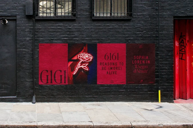 Outdoor image showcases four vibrant red posters on a black brick wall, featuring text and a neon rose, adding an artistic touch to the urban setting.