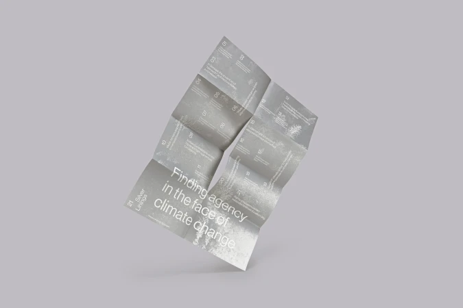 Folded grey printed brochure leaflet floating diagonally against a neutral grey studio background.
