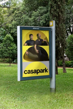 Casapark outdoor advertising poster featuring two men seated against a yellow geometric background in a park setting.