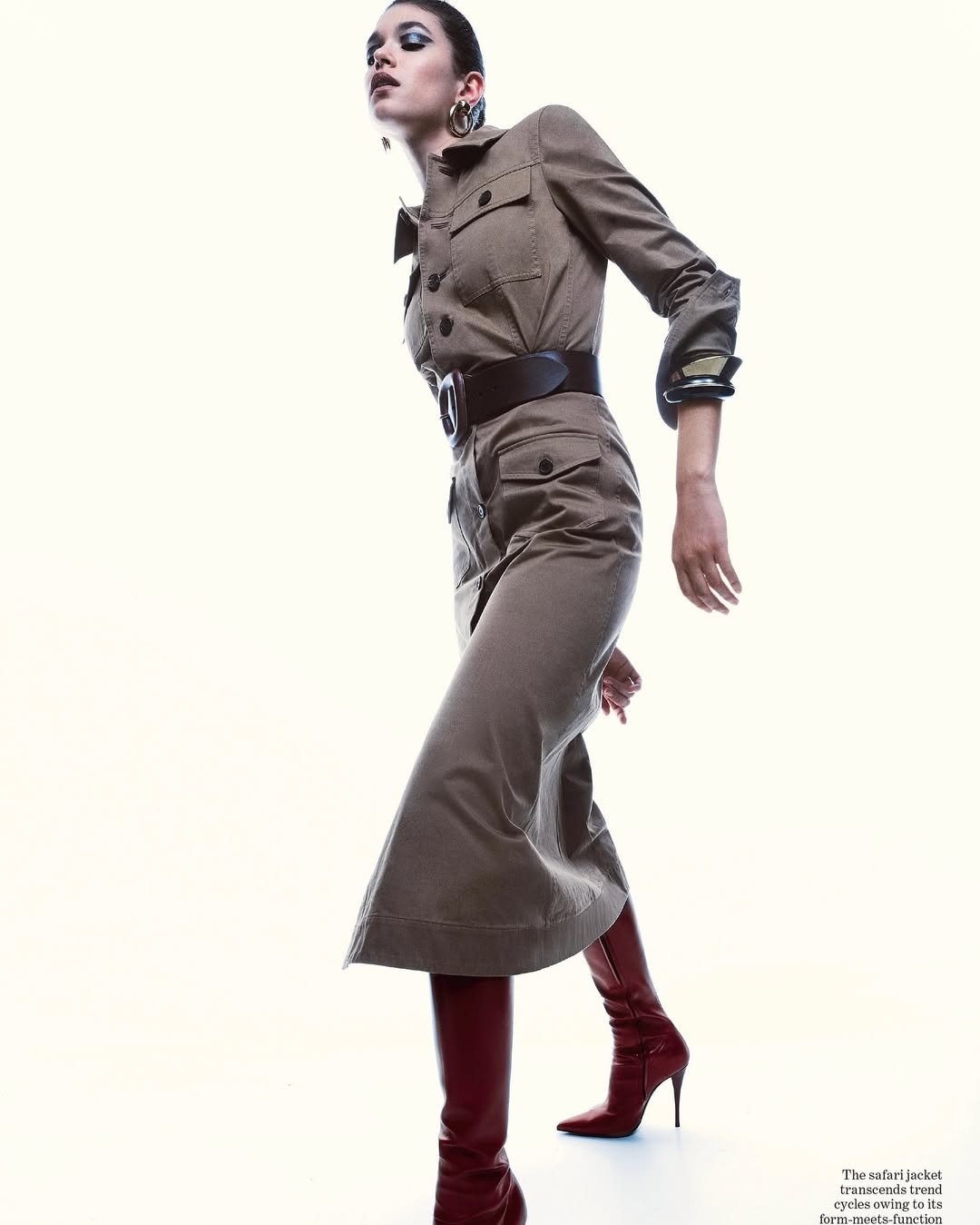 A stylish adult female model in a tan safari-style dress with a wide belt and knee-high red boots strikes a pose against a bright background.