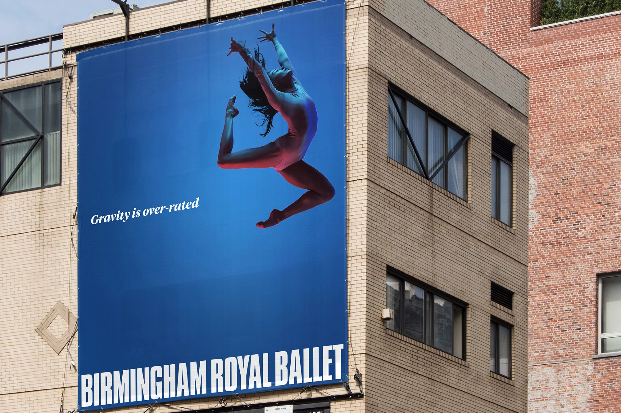 Outdoor billboard advertisement for the Birmingham Royal Ballet, showing a dancer in mid-air against a blue backdrop, mounted on a building.