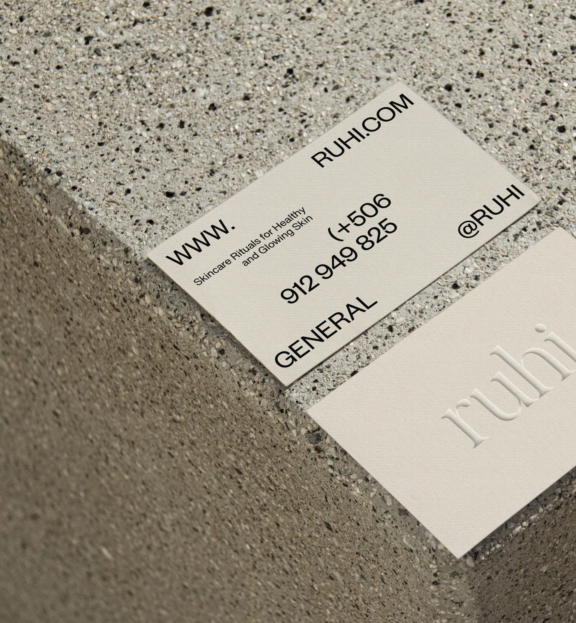 Two business cards featuring the brand name RUHI and website address arranged on a speckled concrete surface in an angled, close-up shot.