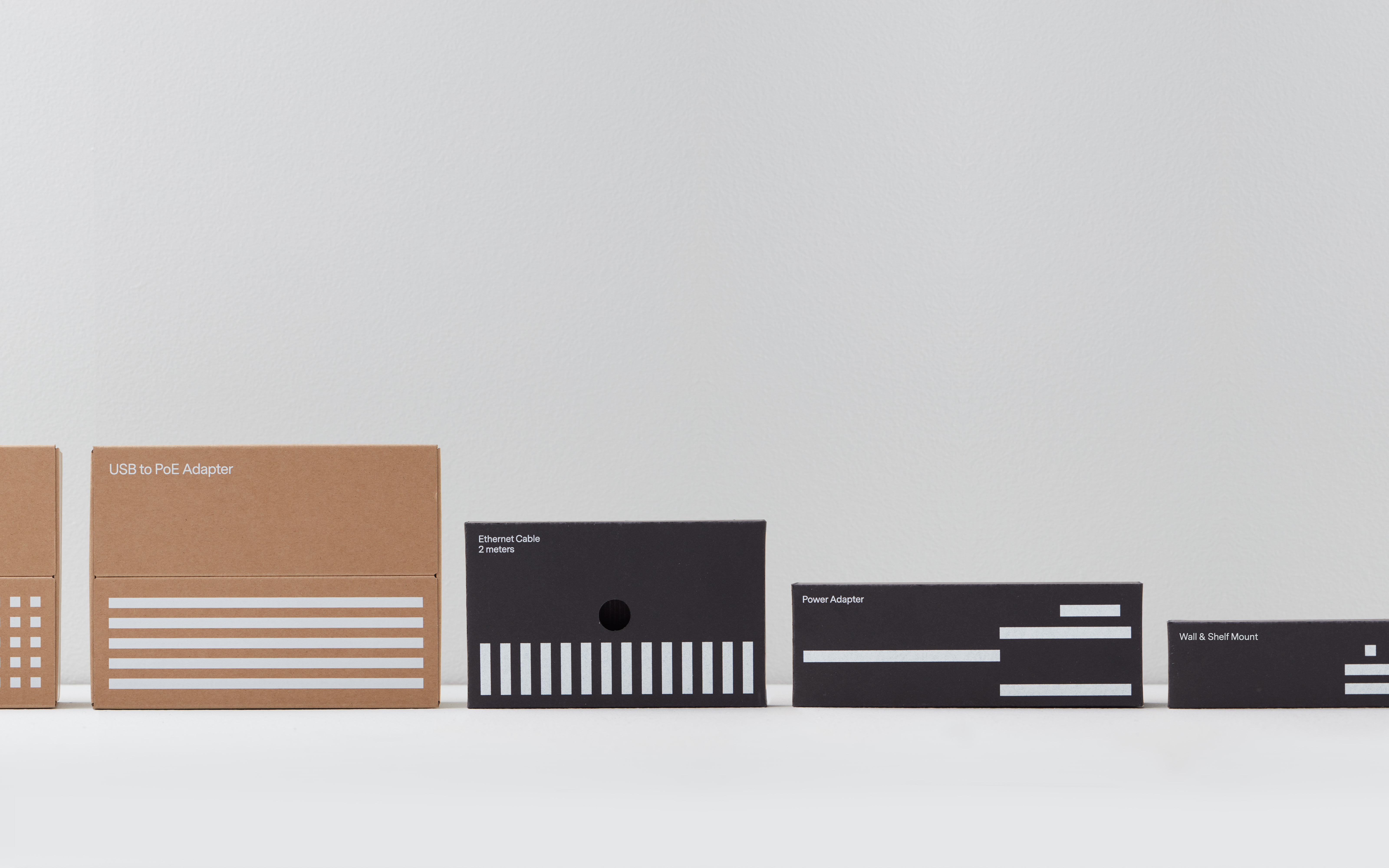 A row of product boxes for electronic accessories, featuring a mix of kraft and black boxes with white text and linear designs.