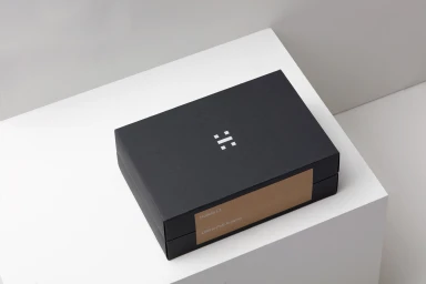 Black product box with white logo sitting on a white geometric studio structure.