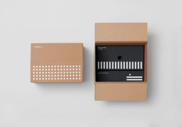 Cardboard packaging boxes for Huddly L1, featuring a closed box and an open shipping carton containing inner black product boxes.