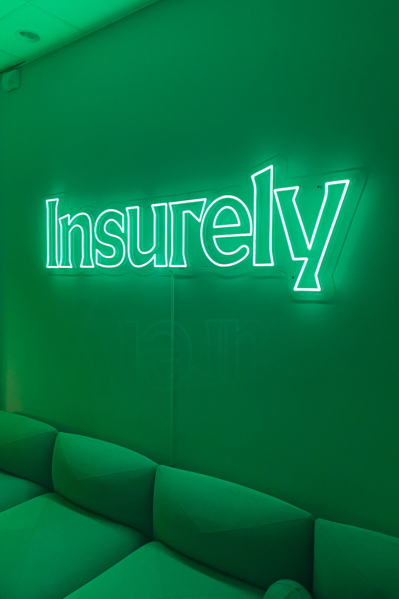 Illuminated 'Insurely' sign on a green wall above a matching green sofa, creating a modern and inviting office space.