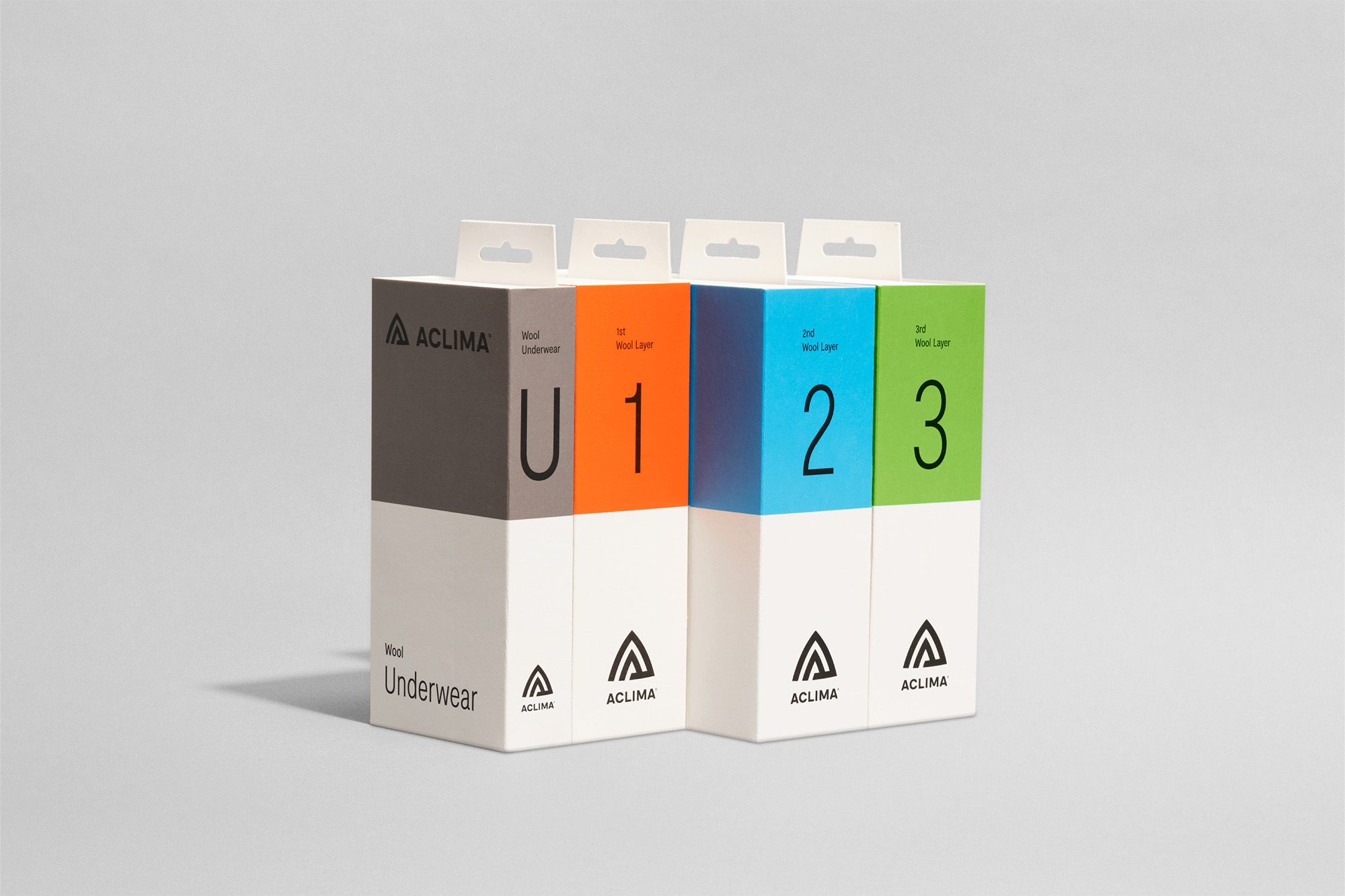 Four Acilma wool underwear packages in gray, orange, blue, and green are stacked together against a light gray background in a studio shot.