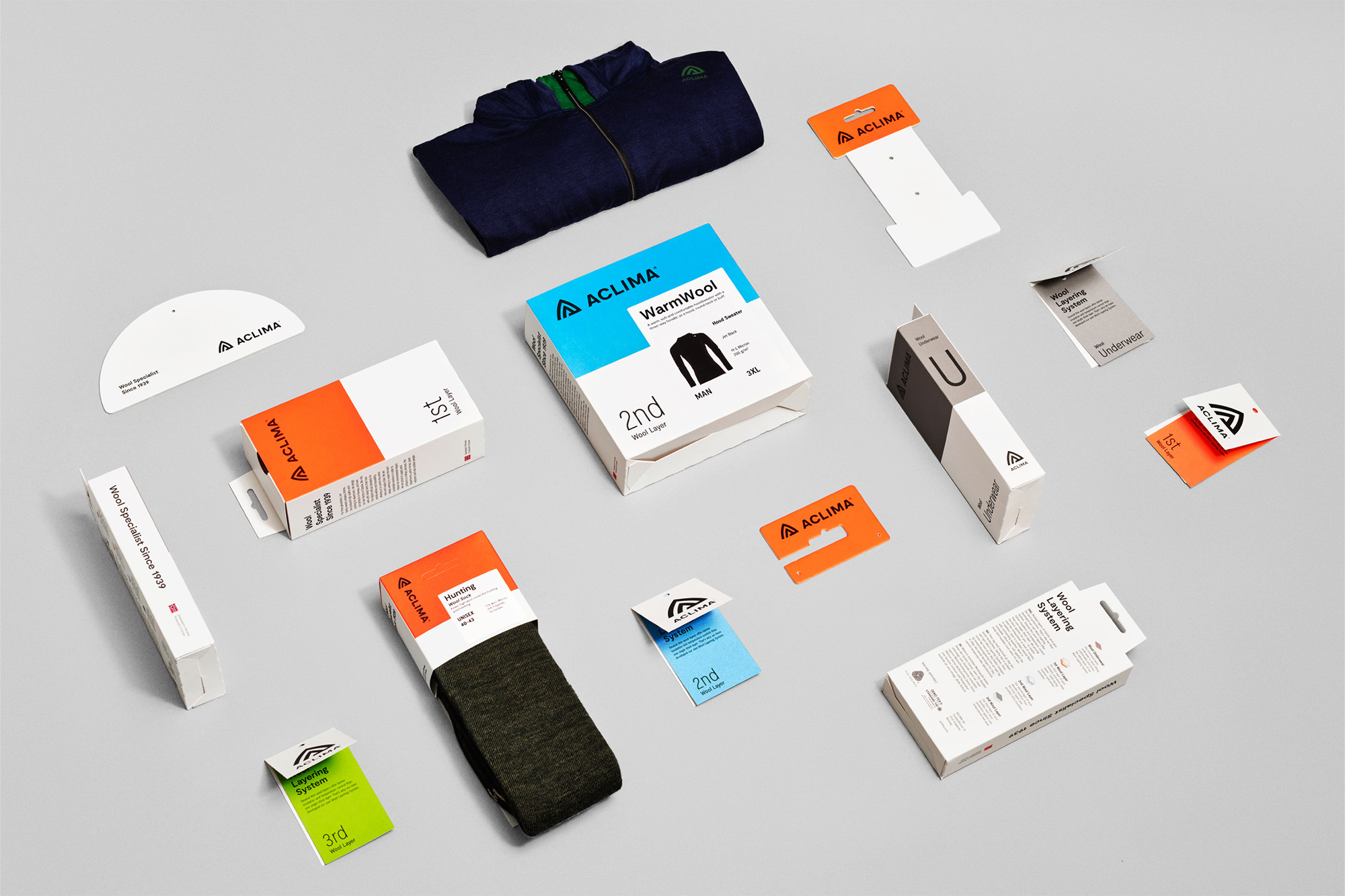 Aclima clothing packaging and products are displayed on a light grey background in a product studio shot for outdoor and fashion industries.