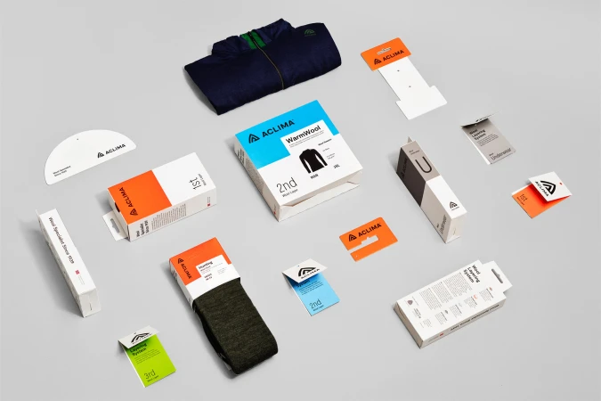 Aclima clothing packaging and products are displayed on a light grey background in a product studio shot for outdoor and fashion industries.