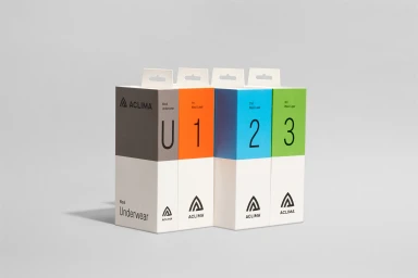 Four Aclima product boxes in grey, orange, blue, and green arranged in a row against a light grey seamless background.
