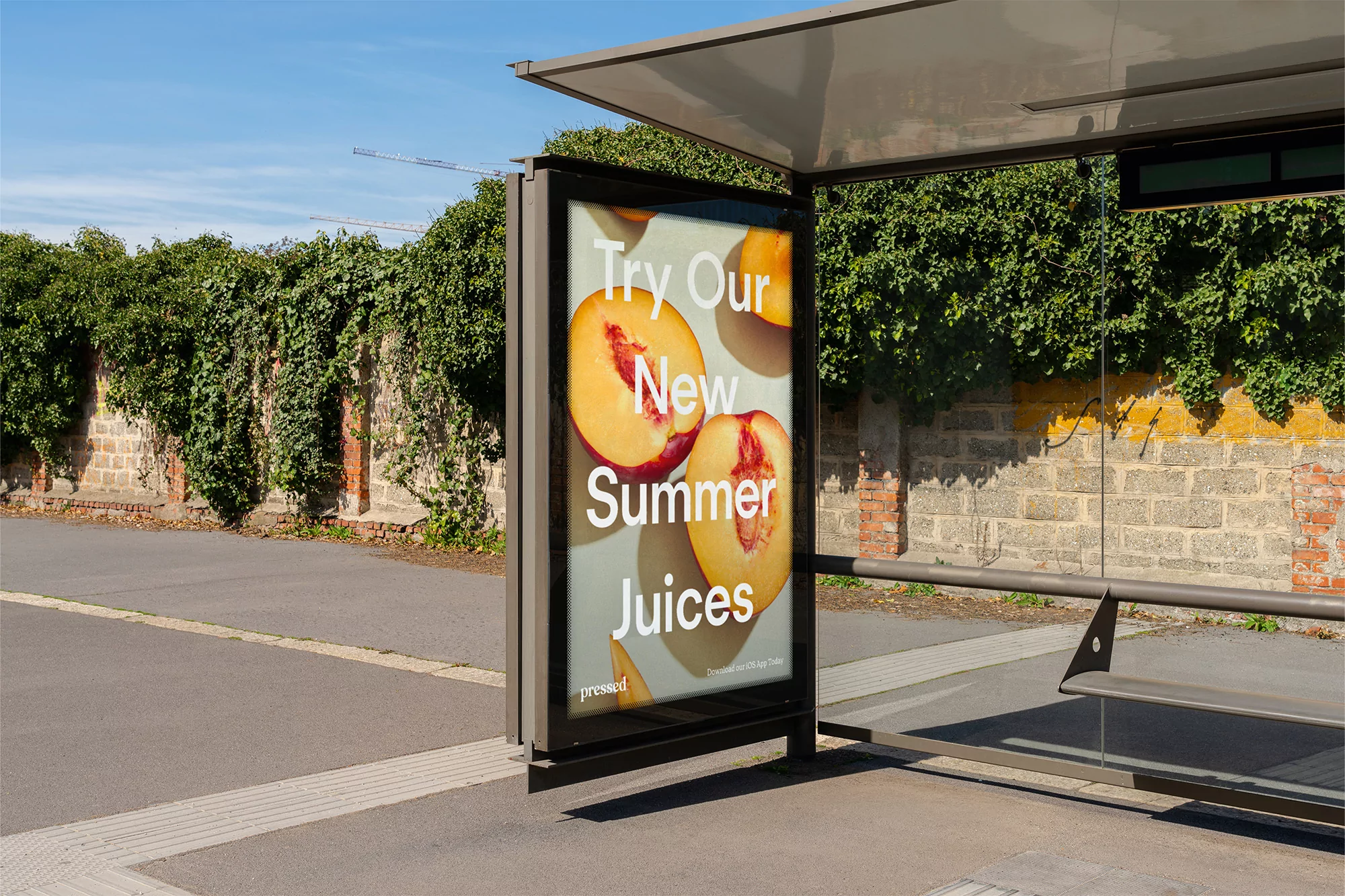 Outdoor advertisement for Pressed brand featuring peach juice, displayed at a bus stop on a sunny day near a brick wall.