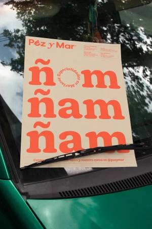 Promotional poster for Pez y Mar restaurant on a green car's windshield under the wiper, featuring the name 'ñam ñam ñam' in bold font.