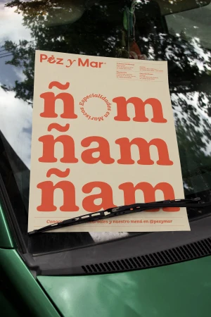 A printed promotional sign with bold orange typography placed on the windshield of a green vehicle.