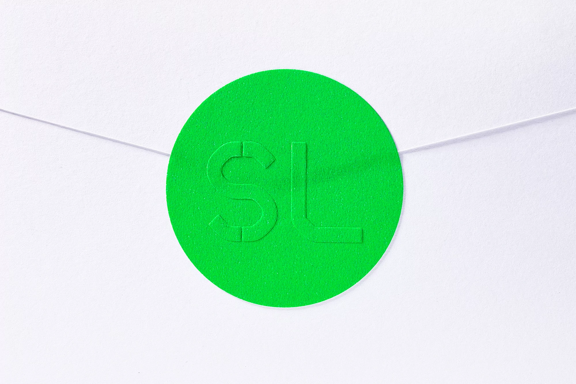 Close-up of a bright green circular sticker with embossed 'SL' letters, affixed to a white envelope; vibrant and minimalist design.