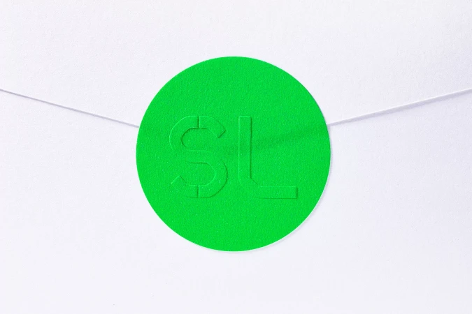 Close-up of a bright green circular sticker with embossed 'SL' letters, affixed to a white envelope; vibrant and minimalist design.